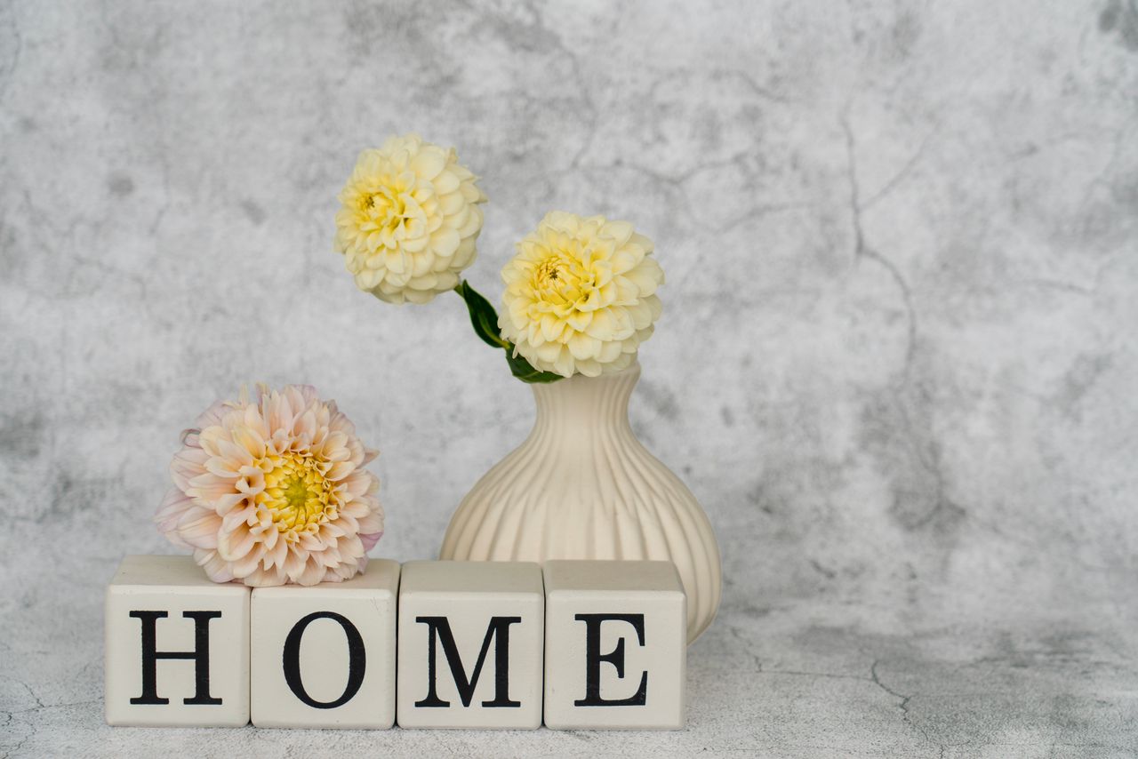 Charming home decor setup with a vase of flowers beside blocks spelling 'HOME' on a textured background.